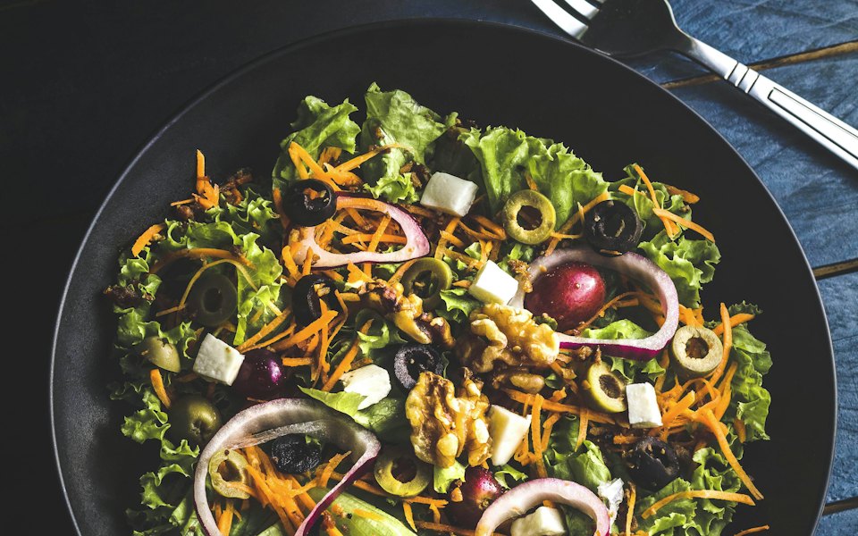 Fresh salad with greens, olives and walnuts on a dark plate