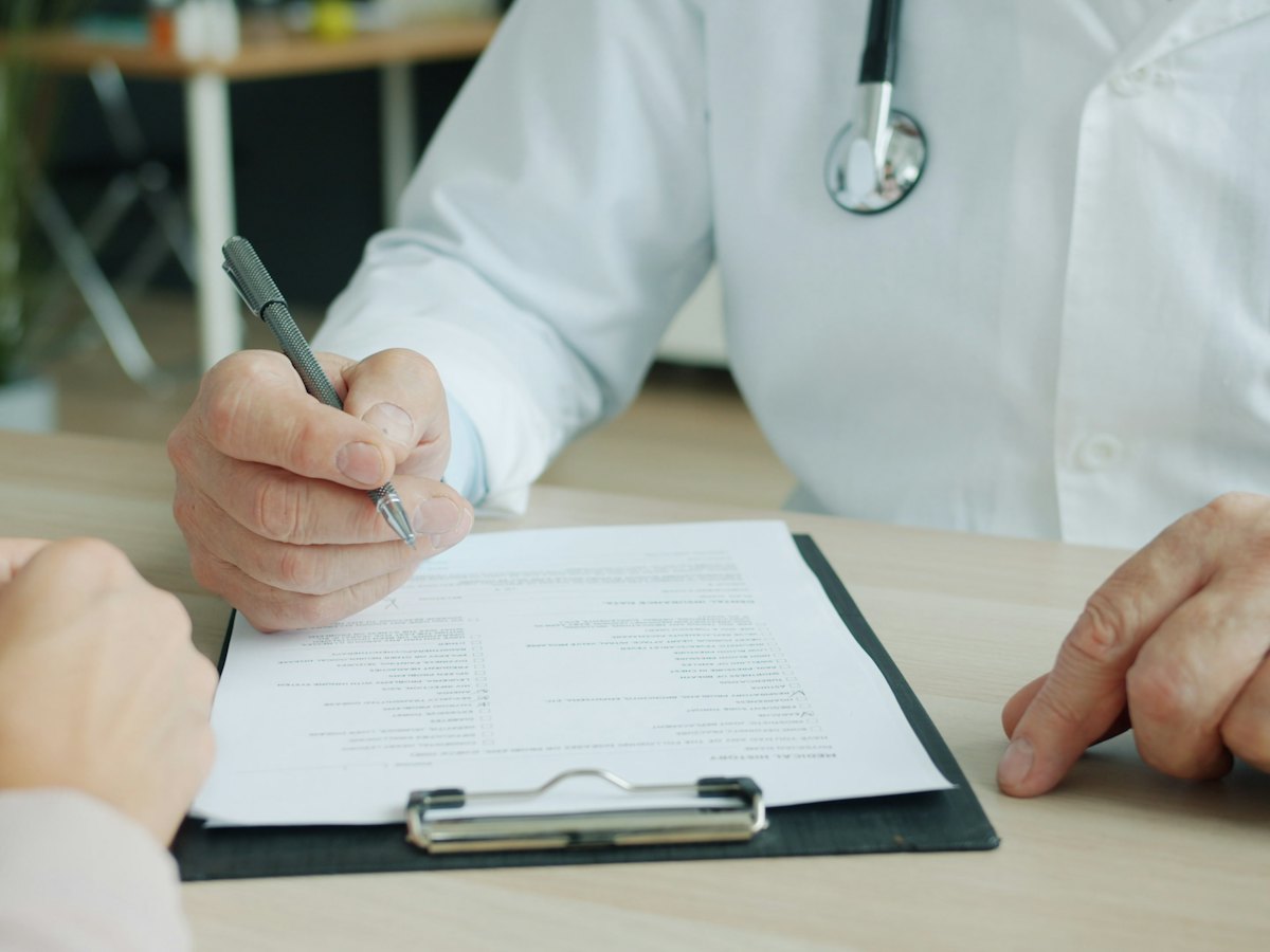 Physician writing notes on a patient chart during a consultation